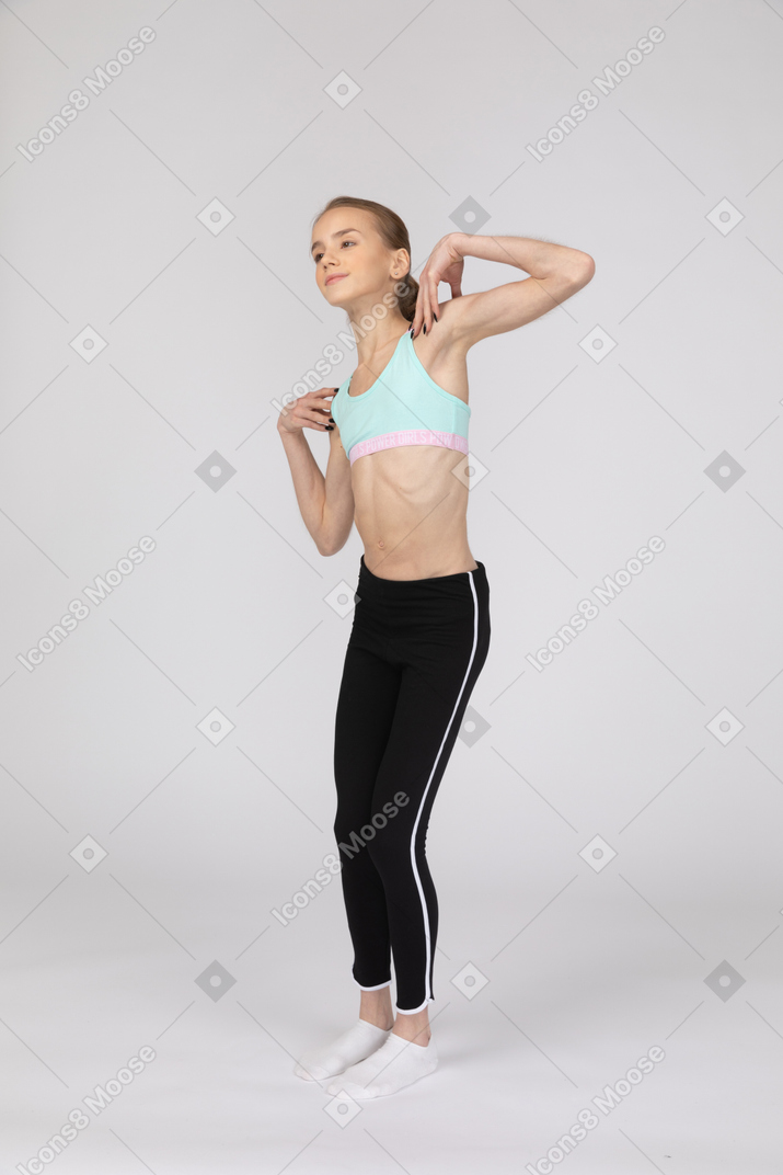 Three-quarter view of a teen girl in sportswear touching her shoulders and tilting left