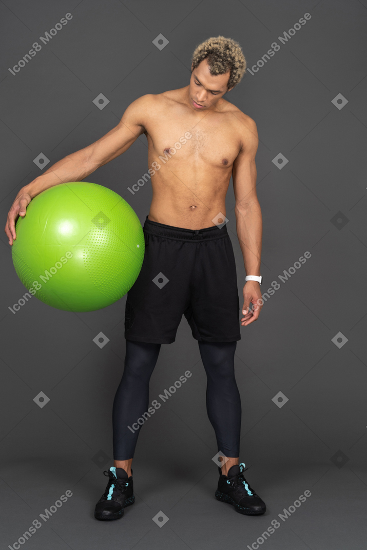 Front view of a shirtless afro man holding a big green gym ball