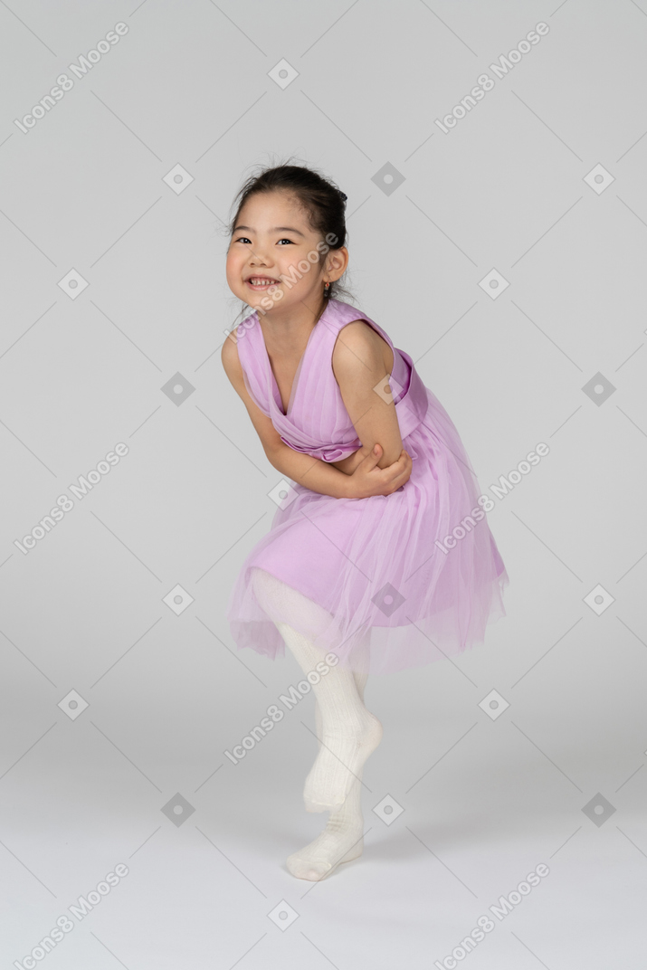 Retrato de uma menina em um vestido de tutu, inclinando-se para a frente enquanto segurava a barriga