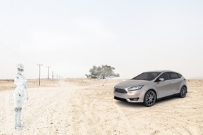 An android and a silver car parked in the middle of a dirt road