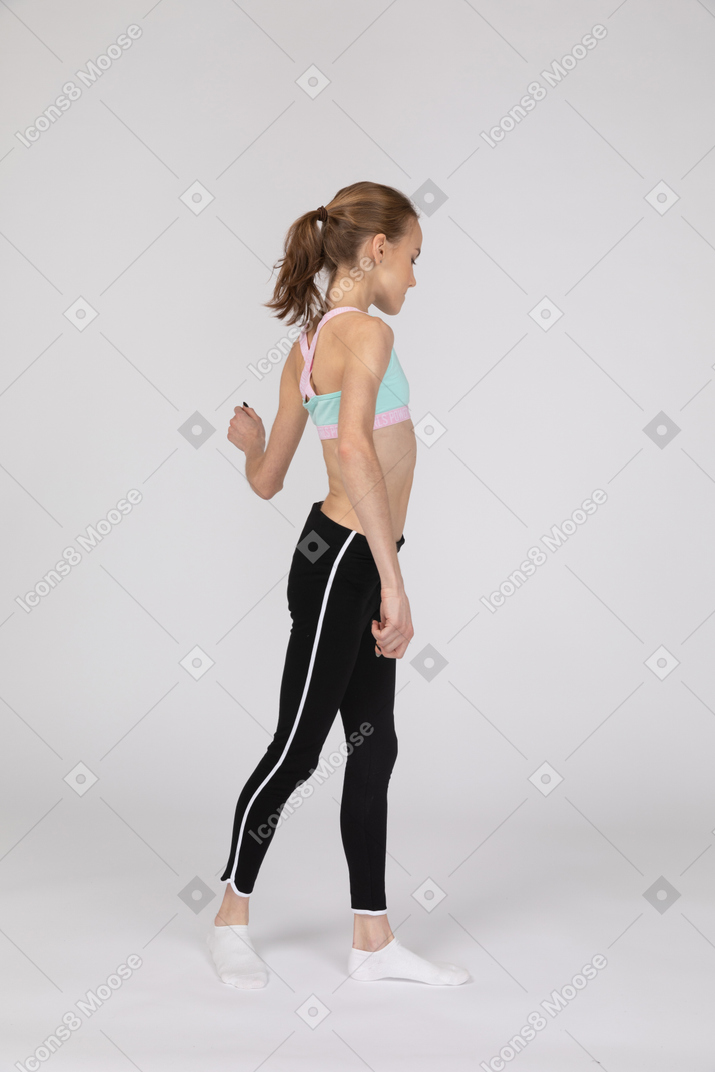 Side view of a teen girl in sportswear walking away while raising her hand