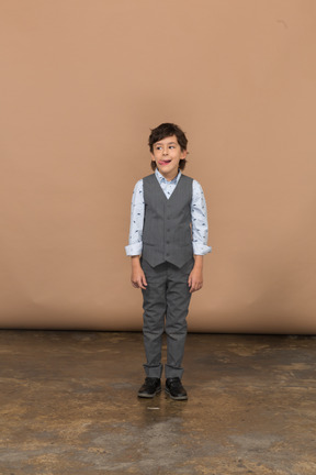 Vista frontal de un chico lindo en traje gris mirando a un lado y mostrando la lengua
