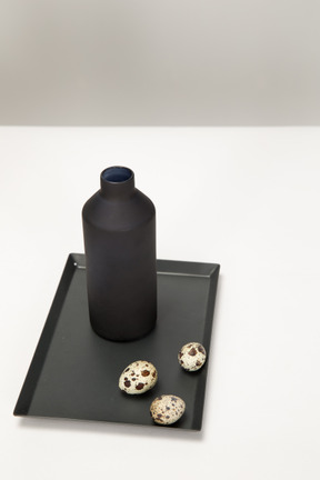 Black vase and quail eggs on the black tray