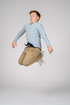 A boy in a blue shirt jumping high with bent knees