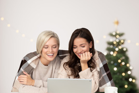 Two young women reading funny stories on laptop