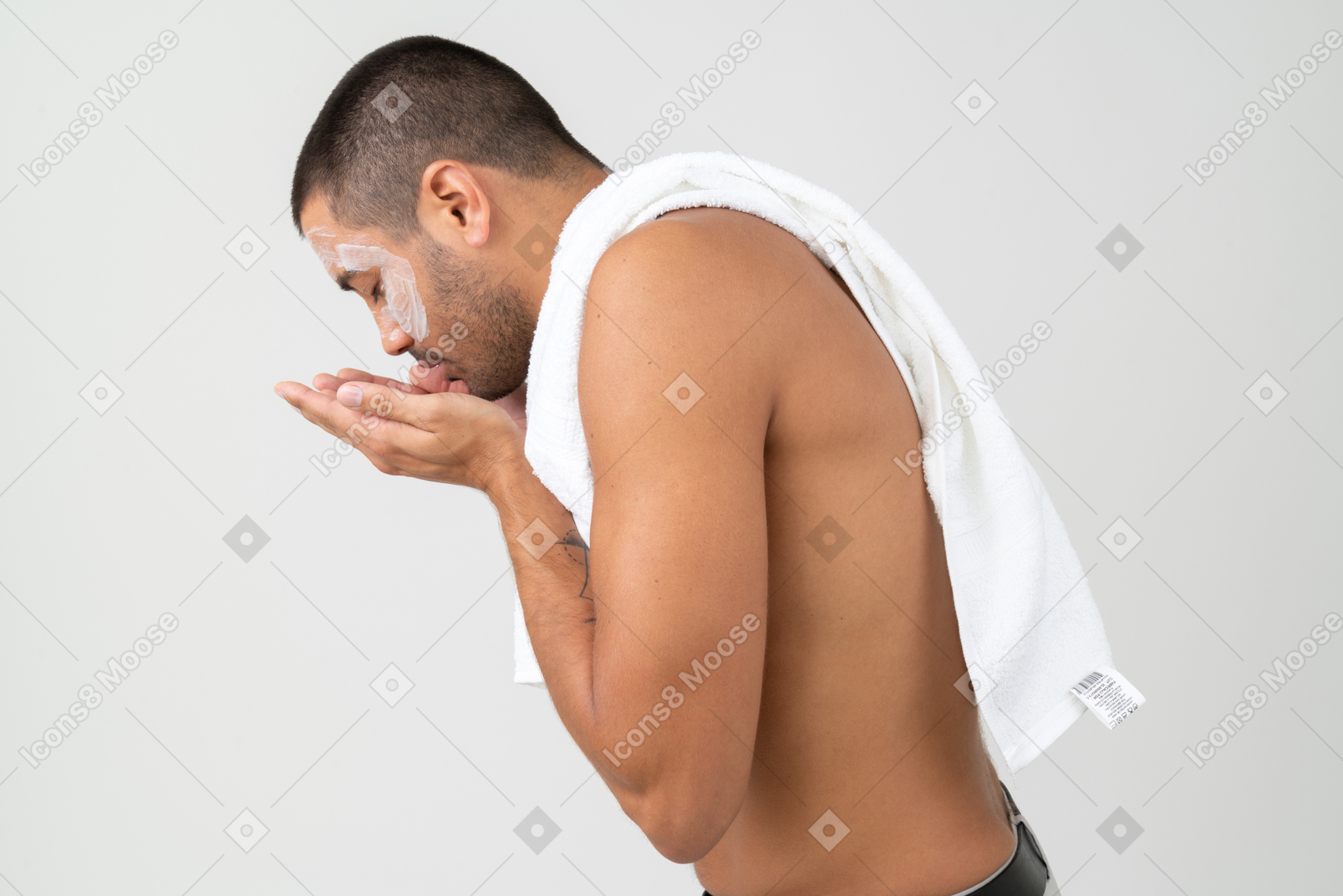 Man with towel on his shoulder washing off facial mask