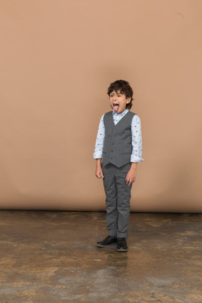 Vista frontal de un niño en traje mirando a la cámara y mostrando la lengua
