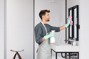A man in an apron cleaning a bathroom mirror