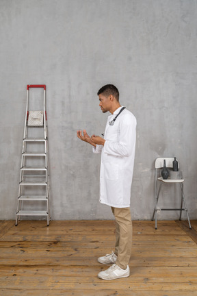 Side view of a young doctor standing in a room with ladder and chair explaining something