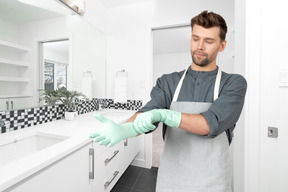 A man in an apron wearing gloves in a bathroom
