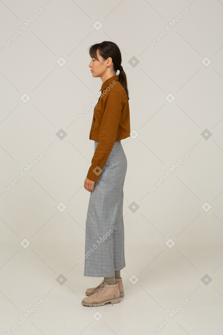 Vista lateral de uma jovem mulher asiática de calça e blusa estreitando os olhos