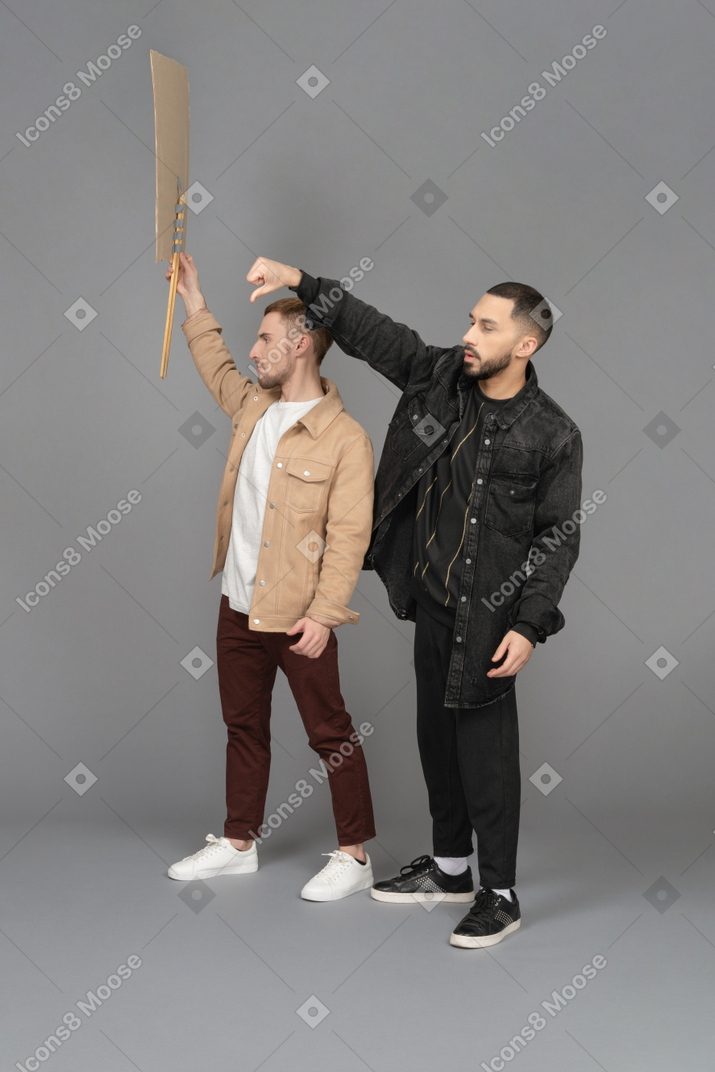 Side view of two young men with a raised billboard looking agitated