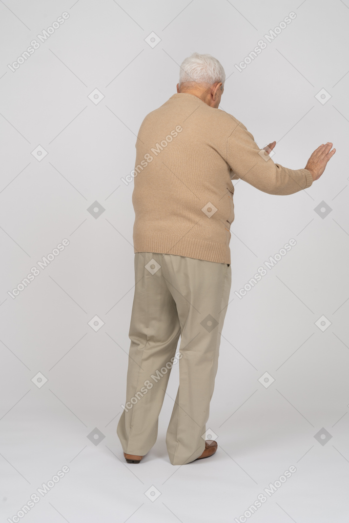Rear view of an old man in casual clothes standing with extended arms