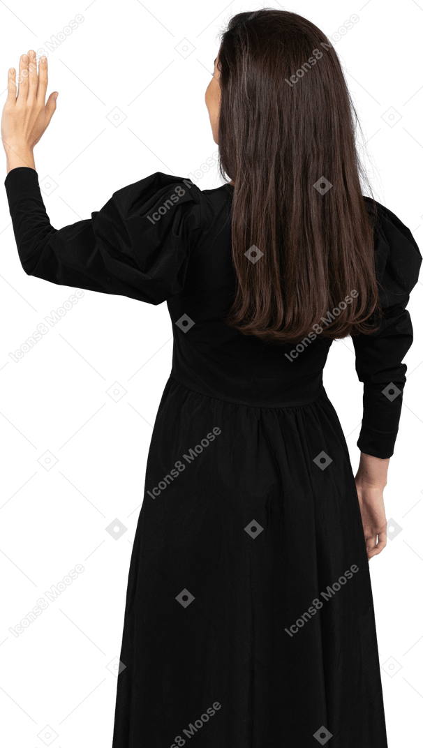 彼女の手を上げている黒いドレスを着た若い女性の背面図