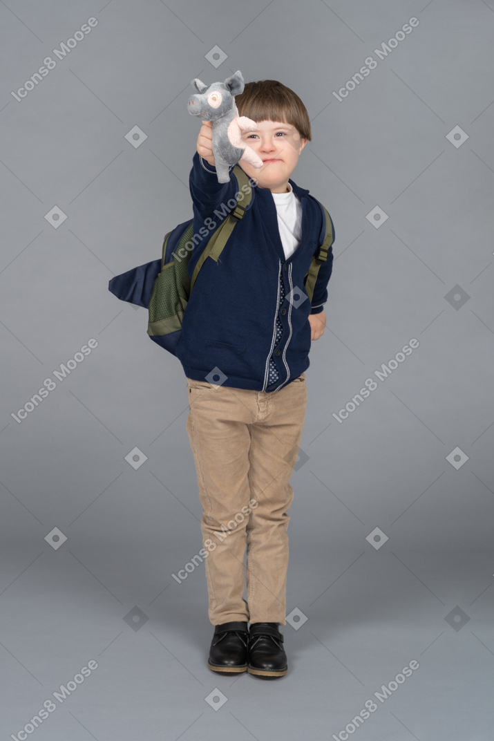 Portrait of a little boy with a backpack holding a piglet plushie