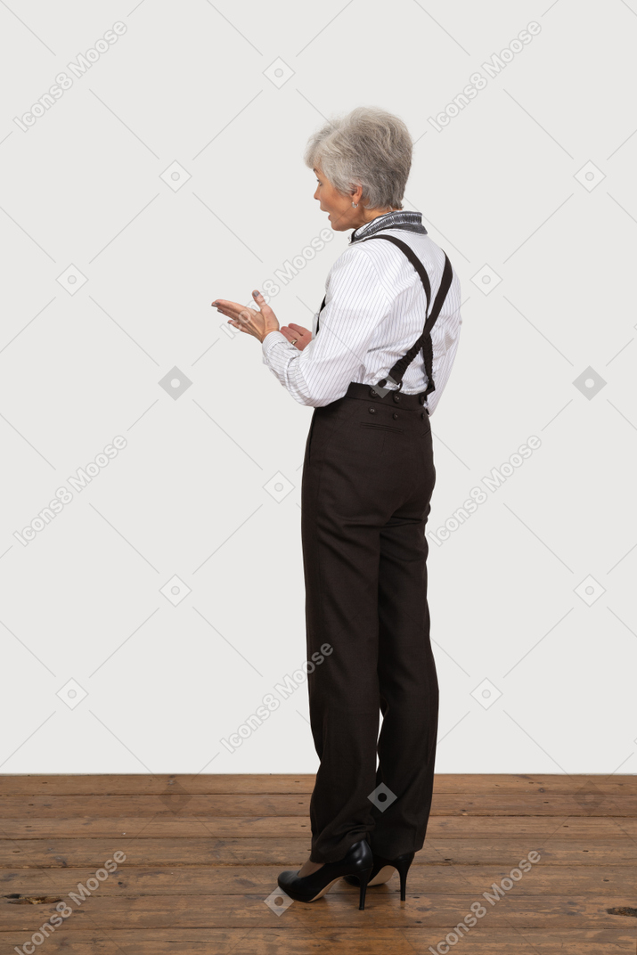 Three-quarter back view of a gesticulating old lady in office clothing