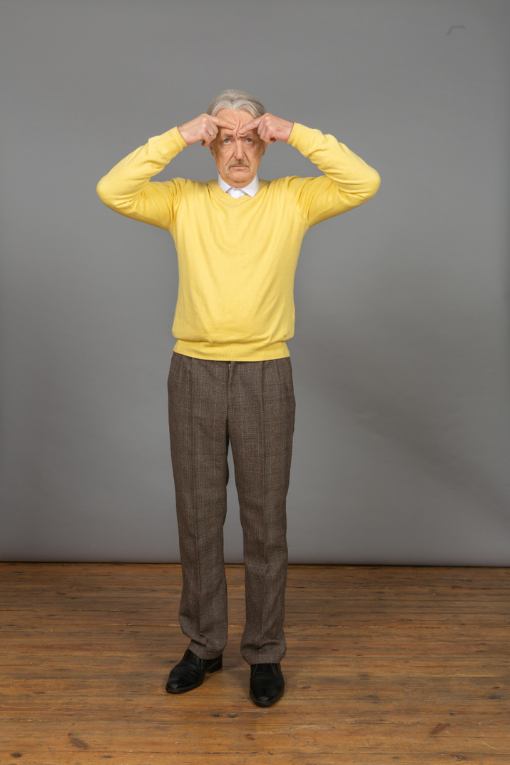 Front view of an old perplexed man in yellow pullover gesticulating actively and looking at camera