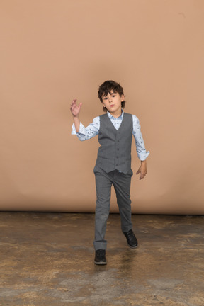 Вид спереди на мальчика в костюме, идущего вперед и машущего рукой