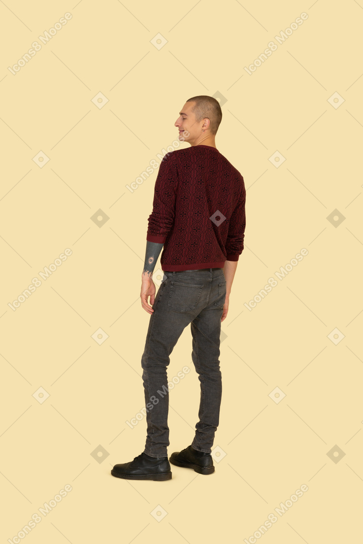Улыбающийся молодой человек в повседневной одежде, вид сзади в три четверти
