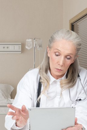 Femme médecin âgé lisant quelque chose sur la tablette qu'elle tient