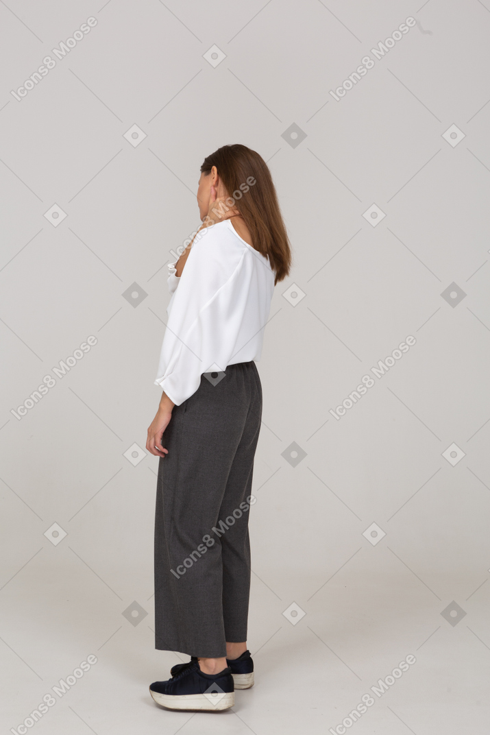 Vista traseira a três quartos de uma jovem com roupas de escritório tocando o pescoço