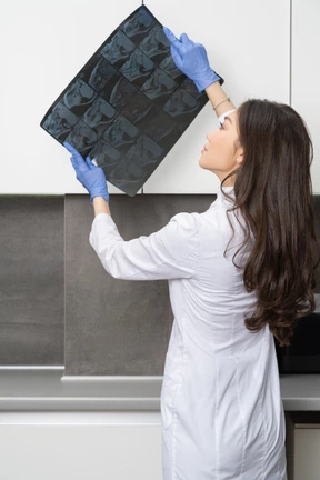 Three-quarter back view of a thoughtful female doctor analyzing x-ray image