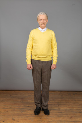 Vista frontal de um velho deprimido vestindo uma blusa amarela e olhando para a câmera