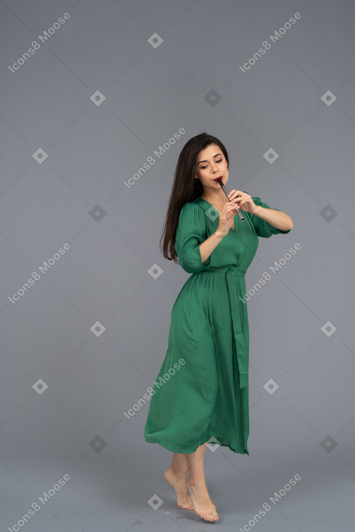 Three-quarter view of a walking young lady in green dress playing the flute