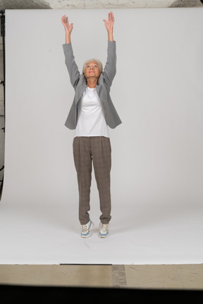 Front view of an old lady in suit standing on toes and raising arms