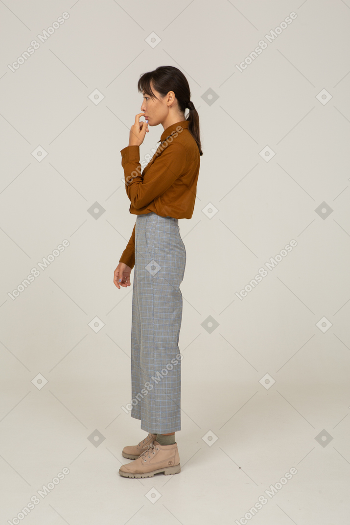 Side view of a young asian female in breeches and blouse touching mouth