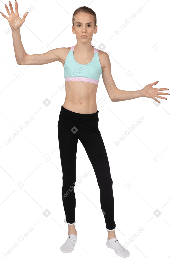Front view of an astonished teen girl in sportswear raising hands