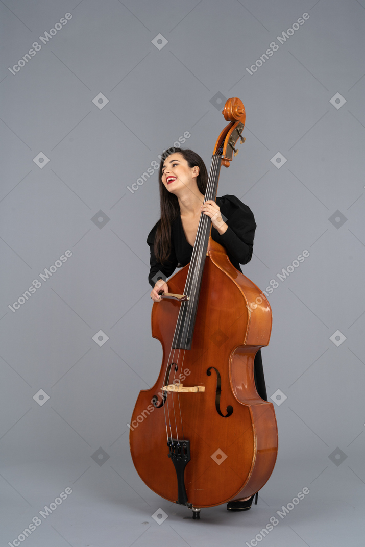 Front view of a smiling young woman in black dress playing the double-bass with a bow