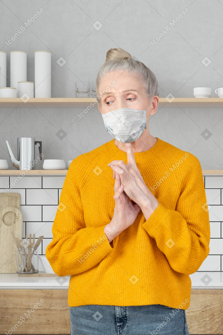 A worried elderly lady standing in the kitchen