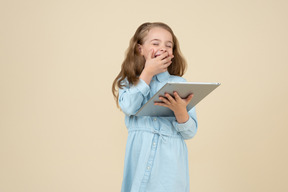 Mignonne petite fille tenant une tablette et rire