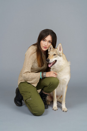 De cuerpo entero de una maestra sentada junto a su perro y mirando a la cámara