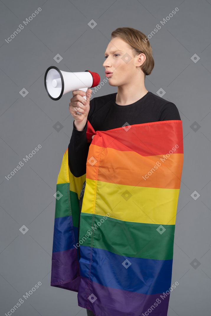 Pessoa com uma bandeira de arco-íris falando em um megafone