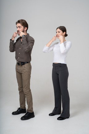 Vista de tres cuartos de una pareja joven en ropa de oficina estirando la boca