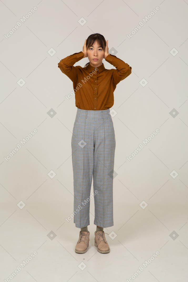 Front view of a young asian female in breeches and blouse touching head