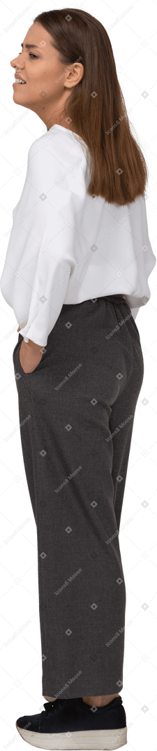 Three-quarter back view of a tired young lady in office clothing putting hands in pockets