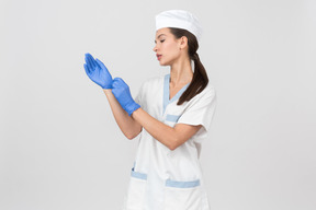 Attraktive krankenschwester in einem medizinischen gewand, das latexhandschuhe überzieht