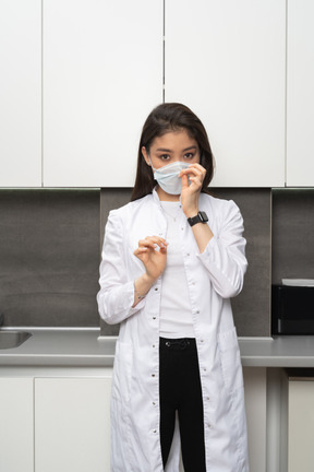 Vue de face d'une femme médecin ajustant son masque de protection et regardant la caméra