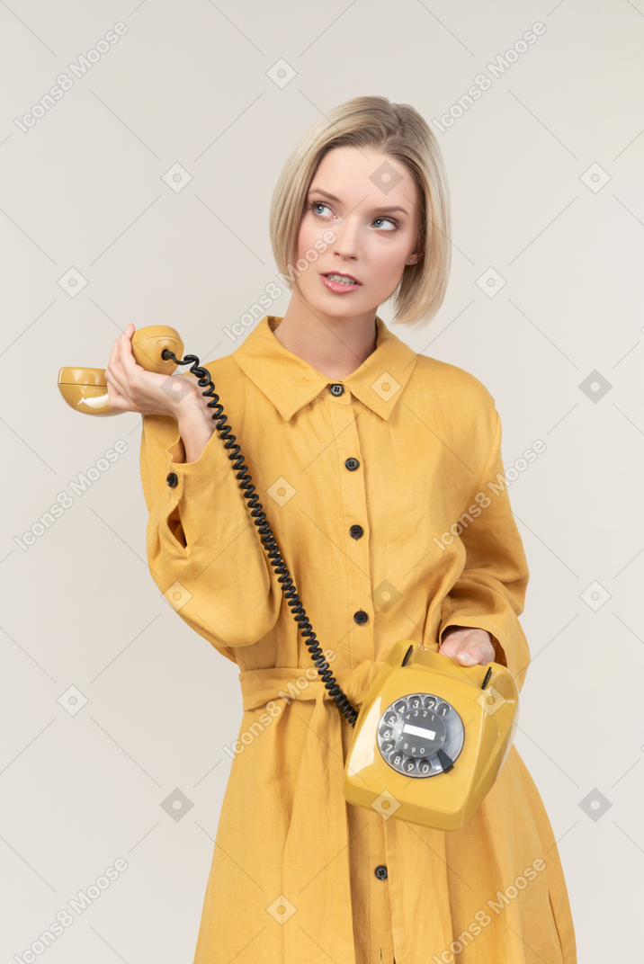 Careless young woman holding yellow old rotary phone