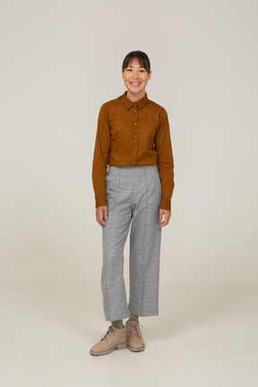 Vista frontal de una mujer asiática joven sonriente en calzones y blusa inmóvil
