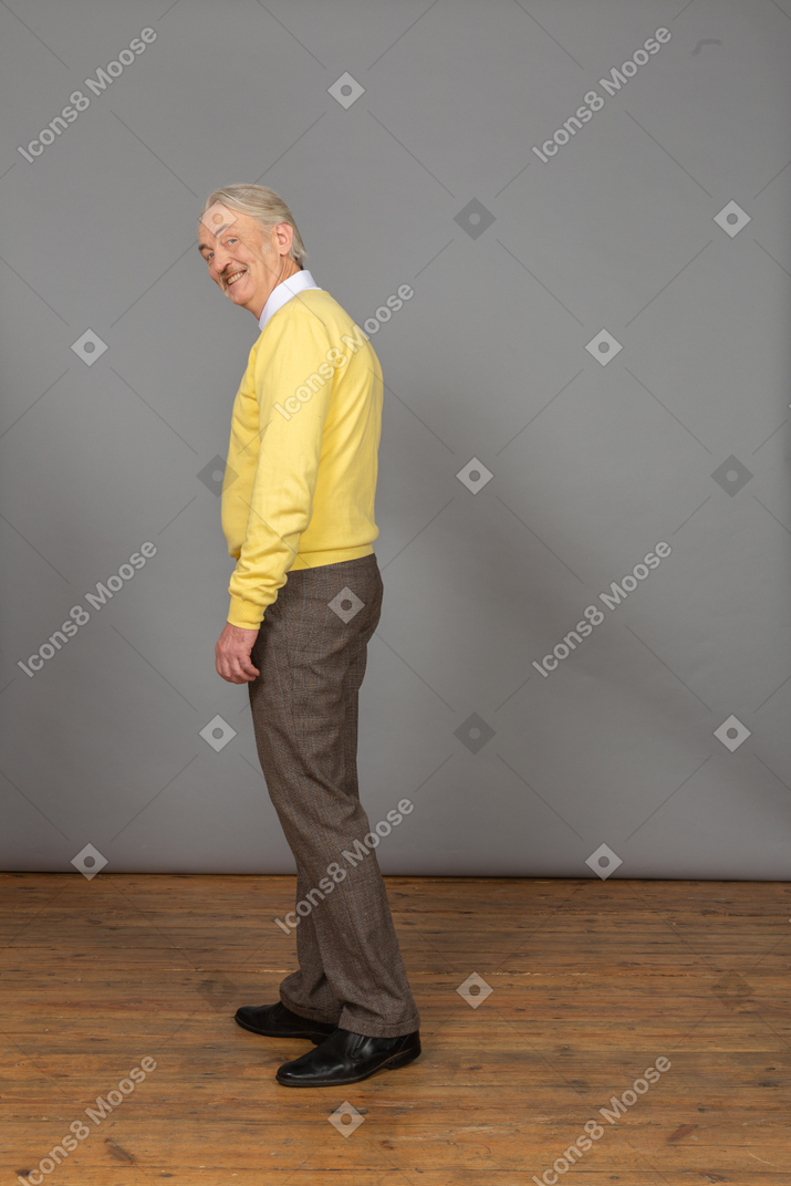 Vista lateral de um homem sorridente, vestindo uma blusa amarela e olhando para a câmera