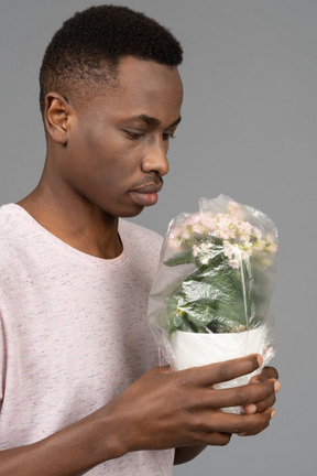 Молодой человек держит цветочный горшок, покрытый пластиком