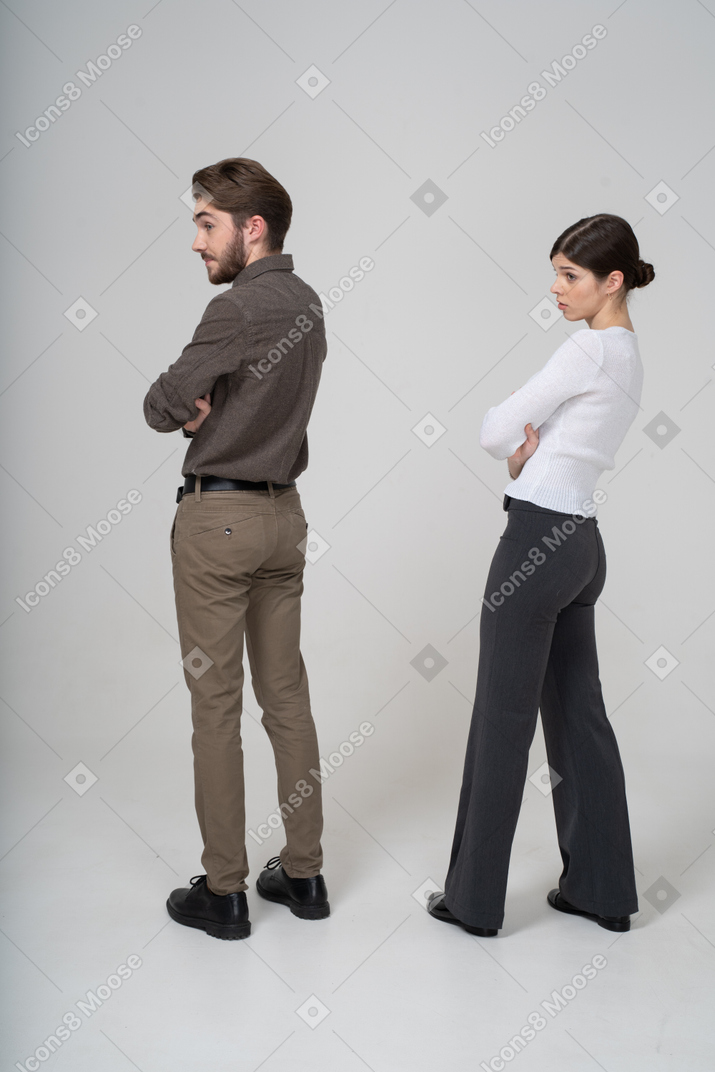 Трехчетвертный вид сзади молодой пары в офисной одежде, скрещивающей руки