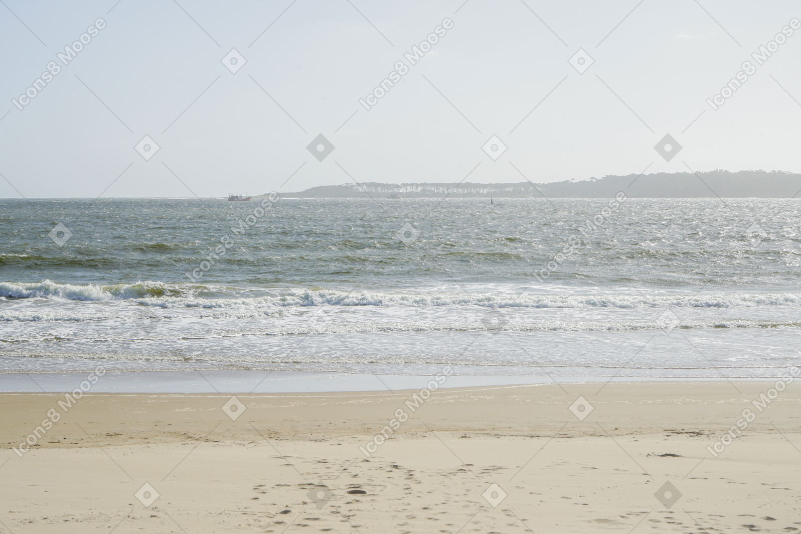 Praia de areia, mar e colinas à distância