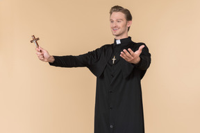 Catholic priest standing half sideways and holding cross