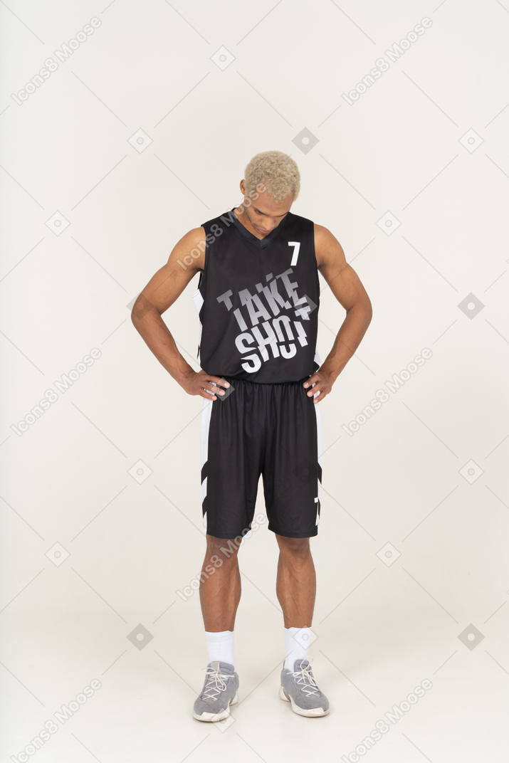 一名年轻男篮球运动员把手放在臀部向下看的前视图