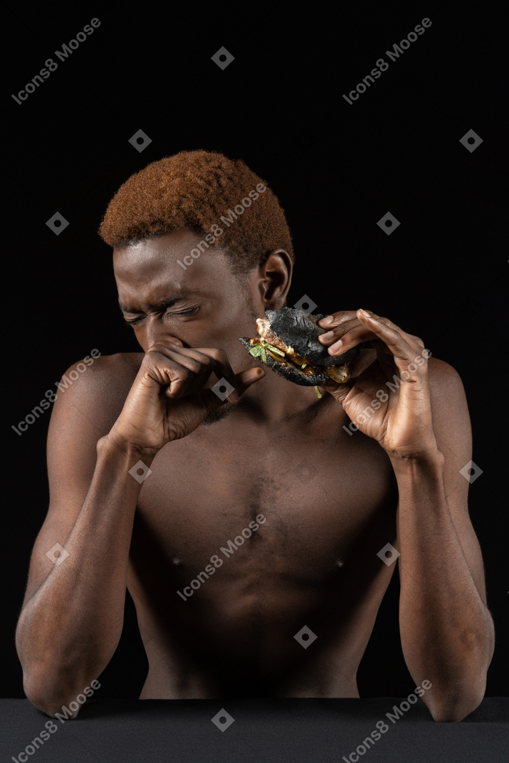 Vista frontal de un joven afro comiendo una hamburguesa